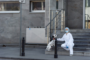 Woman wearing a protective suit is walking alone with a dog outdoors because of the corona virus pandemic covid-19. Female doctor wearing PPE protection suite. Copy space