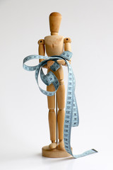Isolated wood adjustable mannequin holding and wrapped in a blue tape measure for a weight loss and plastic surgery beauty concept