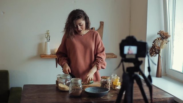 A young girl blogger talks in front of the camera about cooking and at the same time cuts and eats a cucumber