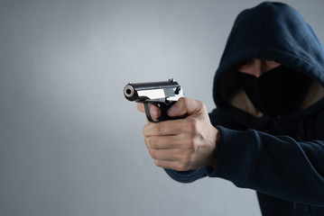 masked man in a hood with a gun in his hands on a black background. place for txt on a gray background