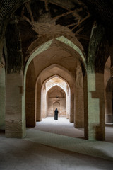 Naklejka premium Isfahan, Iran - May 2019: Unidentified iranian woman in hijab black dress walking along the ancient columns of Jameh Mosque of Isfahan
