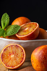 Close-up of oranges sanginas in bowl with mint on rustic wooden table and black background in...