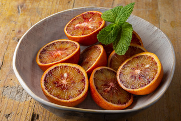 Aerial view of half blood oranges and mint in white bowl, with selective focus, on rustic wooden table, horizontal