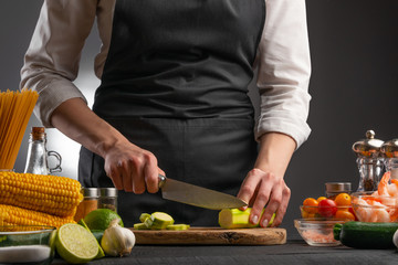 A professional chef cuts zucchini to make a salad with seafood, shrimp. On a gray background with ingredients.
