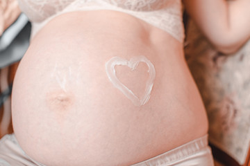 A closeup of a pregnant woman's tummy, with a heart drawn around her belly button.