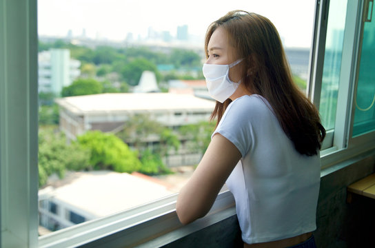 Social distancing concept. Young Asian lady with face mask staying and working at home during quarantine period. Self quarantine. Covid 19 outbreak pandemic.