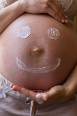 Fototapeta premium Painted happy smiley face on the belly of pregnant woman