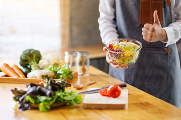 Closeup image of a female chef making and showing thumbs up hand sign while cooking fresh mixed vegetables salad in kitchen