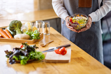 Closeup image of a female chef cooking and holding a bowl of fresh mixed vegetables salad in kitchen