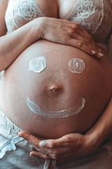 Painted happy smiley face on the belly of pregnant woman