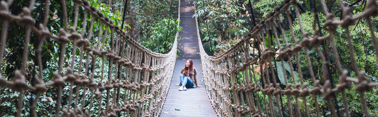 A young woman sitting on wire rope bridge or suspension bridge in the jungle