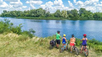Family on bikes cycling outdoors, active parents and kids on bicycles, aerial view of happy family with children relaxing near beautiful river from above, sport and fitness concept
