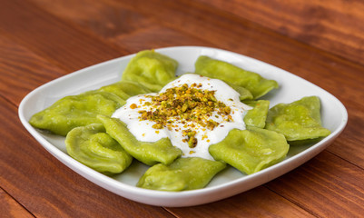 Traditional russian and ukrainian vegetarian green vareniki dumplings, with sour cream and pistachios on a white plate and wooden table. Green dough colored with spinach juice. Side view.