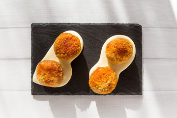 Fried meat balls or croquettes with white sauce on black stone plate on white wooden background. Unhealthy food. Top view on sunny day. Traditional spanish snack.