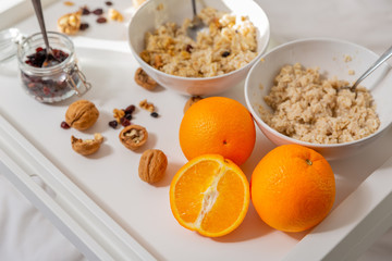 Happy mom and daughter have healthy breakfast on bed in a light bedroom on a sunny morning. Orange juice and oatmeal porridge with nuts and raisins. Healthy food concept. Top view. Close-up