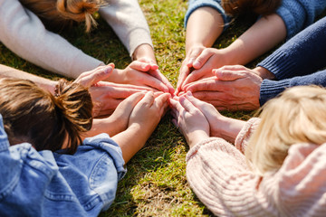 Close up of hands of people sitting outdoors on green grass after doing yoga