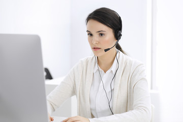 Call center. Casual dressed woman sitting in headset at customer service office. Group of operators at work. Business concept