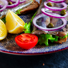 Appetizing smorrebrod with Norwegian herring, lettuce, blue onion, lemon and tomato lies on a...