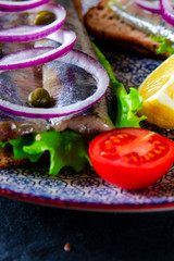 Appetizing smorrebrod with Norwegian herring, lettuce, blue onion, lemon and tomato lies on a wooden board