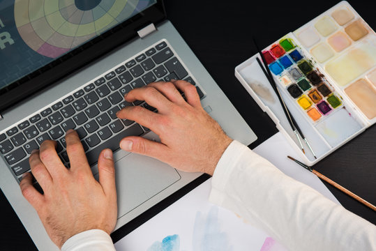 Hands of young man working on the laptop. Concept of graphic designer creating on a dark wood table.