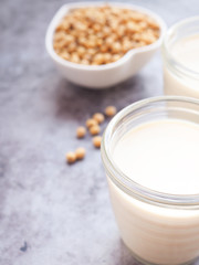 Soymilk in glass with soybeans in a heart-shaped bowl on grey concrete background. Plant protein. Copy space for text.