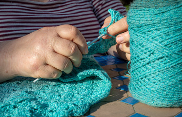 woman making a blue shawl or scarf with crochet hook in garden at home. hobby or pastime.