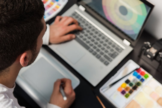 Top view of graphic designer on the workplace creating on the laptop. Workplace with tools, camera, graphic tablet and watercolors. Studio design concept. Blur tools
