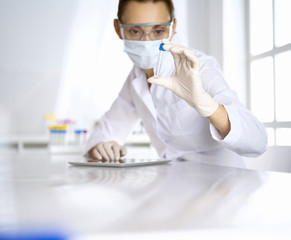 Female laboratory assistant in mask analyzing test tube with blue liquid. Medicine, health care and virus pandemic protection