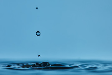 Gotas de agua cristalina chapoteando en una superfície de agua calmada y formando ondas circulares