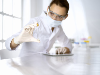 Female laboratory assistant in mask analyzing test tube with blue liquid. Medicine, health care and virus pandemic protection