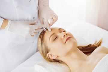 Fototapeta na wymiar Beautician doctor doing beauty procedure with syringe to caucasian female face in synny room. Cosmetic medicine and surgery, beauty injections concept