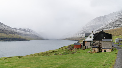 Fototapeta na wymiar Bour, Faroe Islands - August 2019: A small settlement village overlooking a fjord surrounded by green mountains