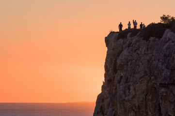 People watching pretty sunset over cliffs and sea in Menorca, Spain