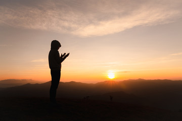 Fototapeta premium Silhouette of Christian woman praying worship at sunset. Christian Religion concept background. Hands in prayer. worship god with religion concept.