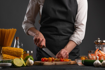 The chef cuts cherry tomatoes to make a fresh salad with shrimp, seafood. Cookery and recipe book. Restaurant cuisine. Recipes