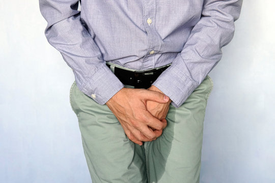 adult man holds hands the groin area and trousers wet from urine. Urinary incontinence concept. Wet person. Blue background. Health problem. Medical concept.