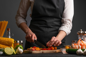 The chef cuts cherry tomatoes to make a fresh salad with shrimp, seafood. Cookery and recipe book. Restaurant cuisine. Recipes