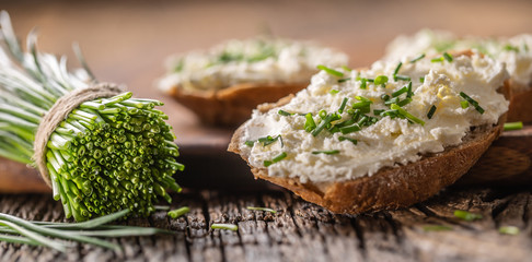 Chive cream cheese spread on a bread slices next to bunch of freshly cut chives on a rustic wood and chopping board