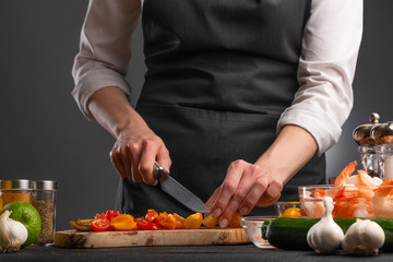 The chef cuts cherry tomatoes to make a fresh salad with shrimp, seafood. Cookery and recipe book. Restaurant cuisine. Recipes