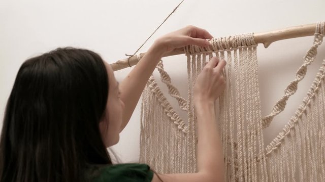 woman weaves macrame on a stick.