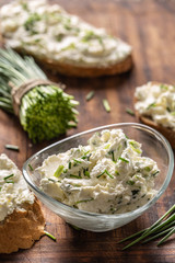 Portrait of a bowl of homemade cream cheese spread with chopped chives surrounded by bread slices with spread and a bunch of freshly cut chives