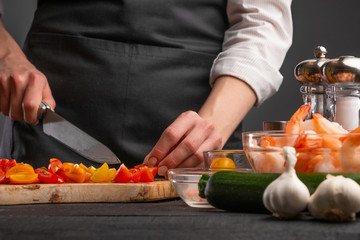 Cooking StirFry vegetables with shrimp. Chef slices cherry tomatoes, on a gray background with shrimp. Seafood