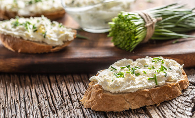 Slices of crusty bread with a cream cheese spread and freshly cut chives on a vintage wooden cutting board - obrazy, fototapety, plakaty