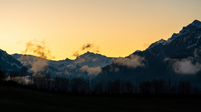  landscape picture of mountain tange in Switzerland, St. Gallen, in the morning sun with clouds infront of dark silhouettes