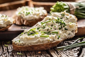 Close-up of bread slice with traditional Slovak bryndza spread made of sheep cheese with freshly cut chives placed on rustic wood