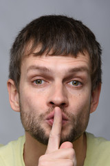 Portrait of a man of European appearance who put a finger to his mouth, gesture of silence, close-up