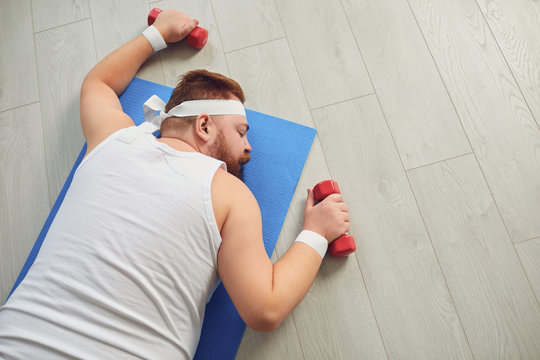 A lazy fat man is sleeping with dumbbells in training on the floor in the house.