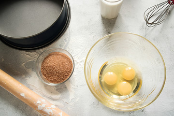 Eggs in a glass bowl, sugar, a glass of milk, rolling pin and a pie dish