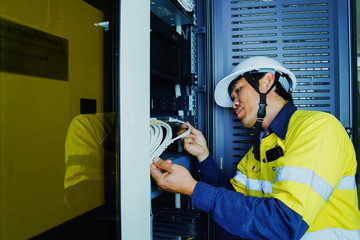 Engineer in yellow uniform, wearing a white safety helmet, checking communication system, big data...