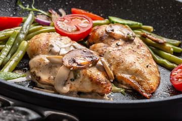 Grilled chicken fillet with a creamy mushrooms sauce, green beans and tomatoes in a skillet close up